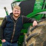 Kaleb Cooper standing in front of John Deere tractor