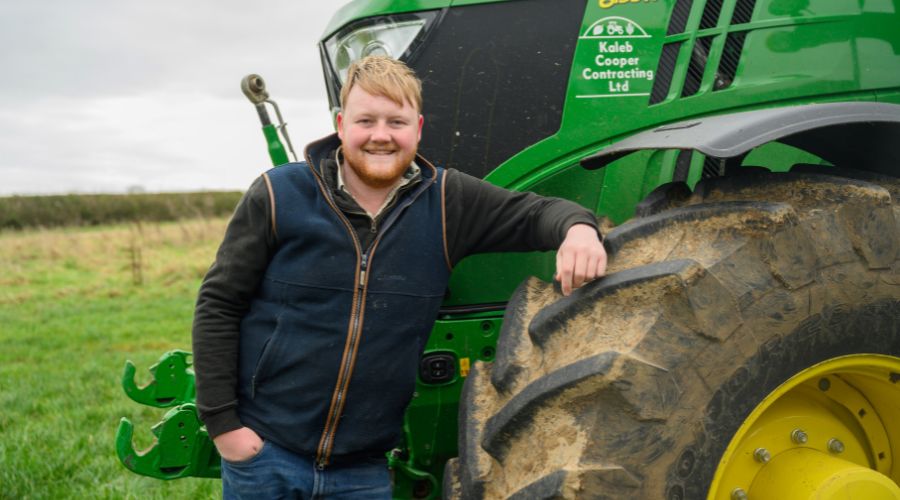 Kaleb Cooper standing in front of John Deere tractor