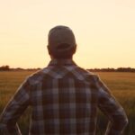farmer facing away from camera looking out over field at sunset