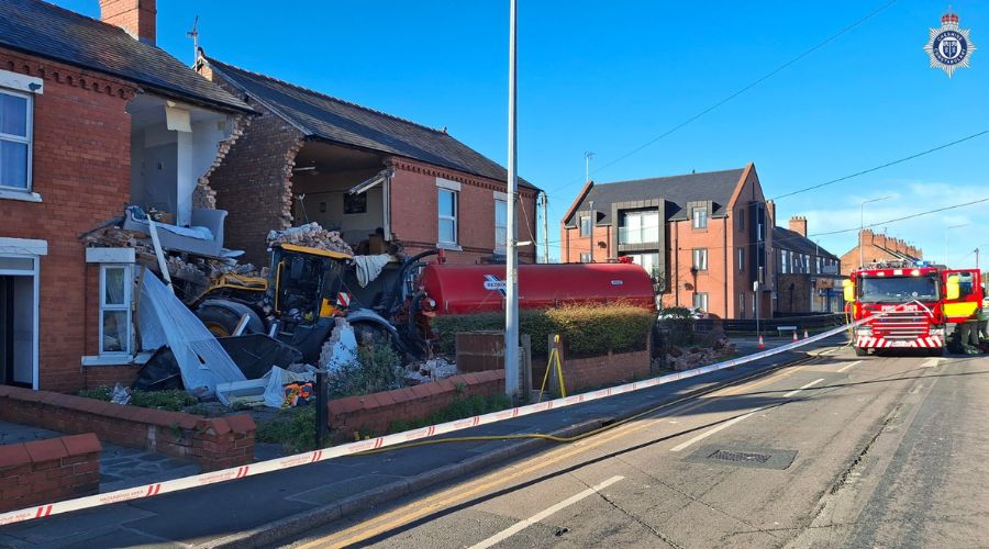 JCB tractor pulling slurry tanker, crashed into two houses, knocking the facade out of both houses. In the background, a fire engine and cordon 